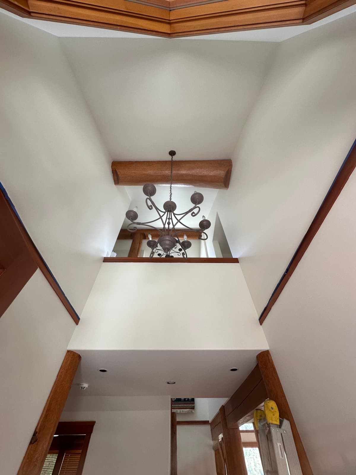 Freshly painted crisp white walls and ceiling in a log home stairwell hallway with a natural log post, wood trim and a wrought-iron chandelier