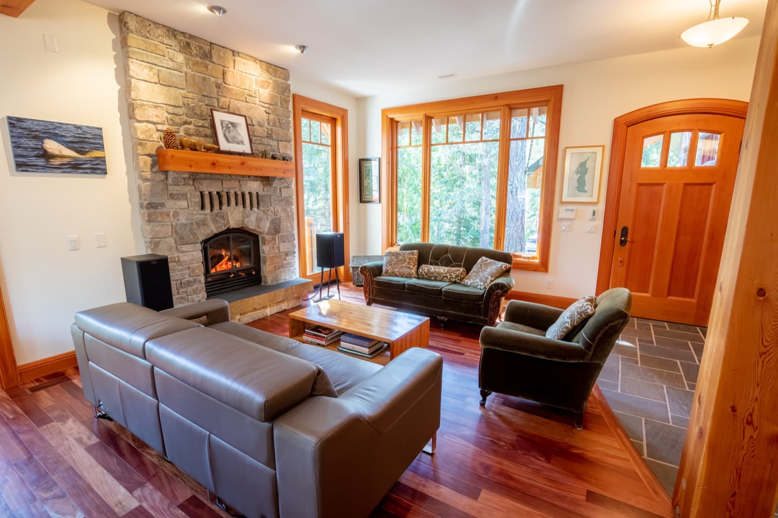Warm timber-frame living room with floor-to-ceiling stone fireplace, fir-trimmed windows and door, freshly painted cream walls